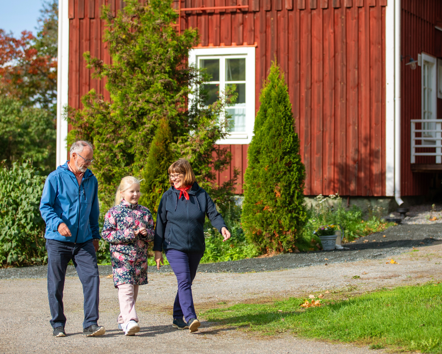 Isovanhemmat kulkevat lapsenlapsen kanssa vanhan talon edessä